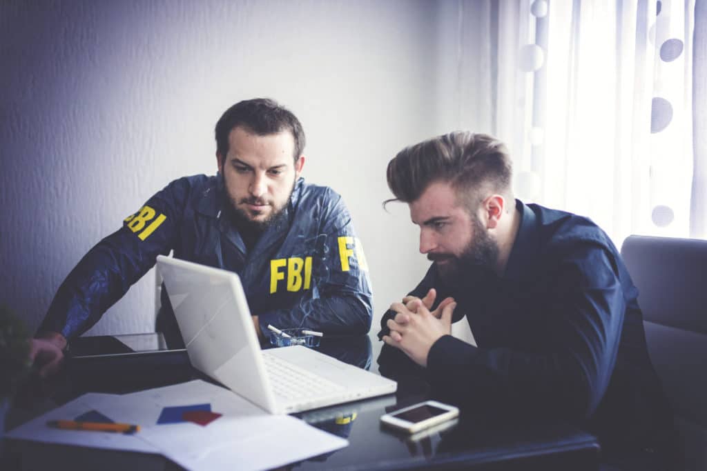 Two male FBI agents are looking at the footage before they create one of their FBI search warrants.